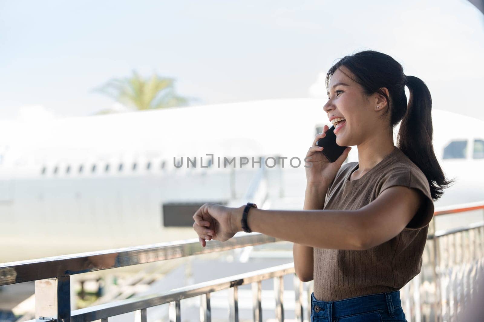 A young woman happily chatting on her phone at the airport, showcasing the blend of travel excitement and professional life.