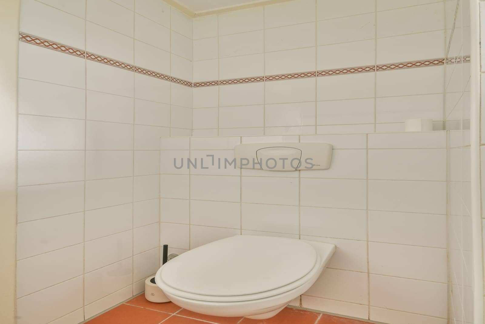 A clean and simple bathroom featuring a modern toilet against white tiled walls, accented with a subtle border design. Functional and uncluttered space.