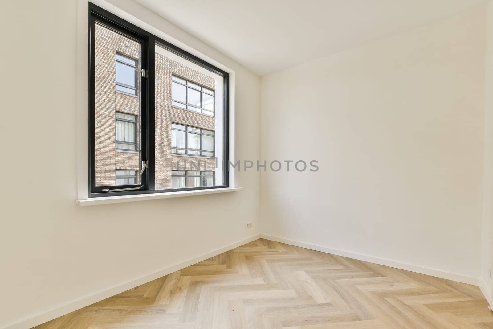 Bright, spacious interior showcasing a large window, providing a view of the outside. The minimalist design features light-colored walls and herringbone flooring.