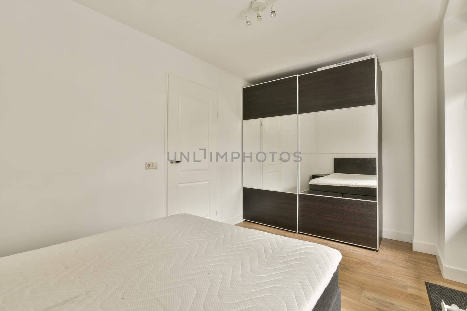 A minimalist bedroom featuring a sleek wardrobe and a simple bed layout. The neutral palette enhances the serene ambiance of the space.