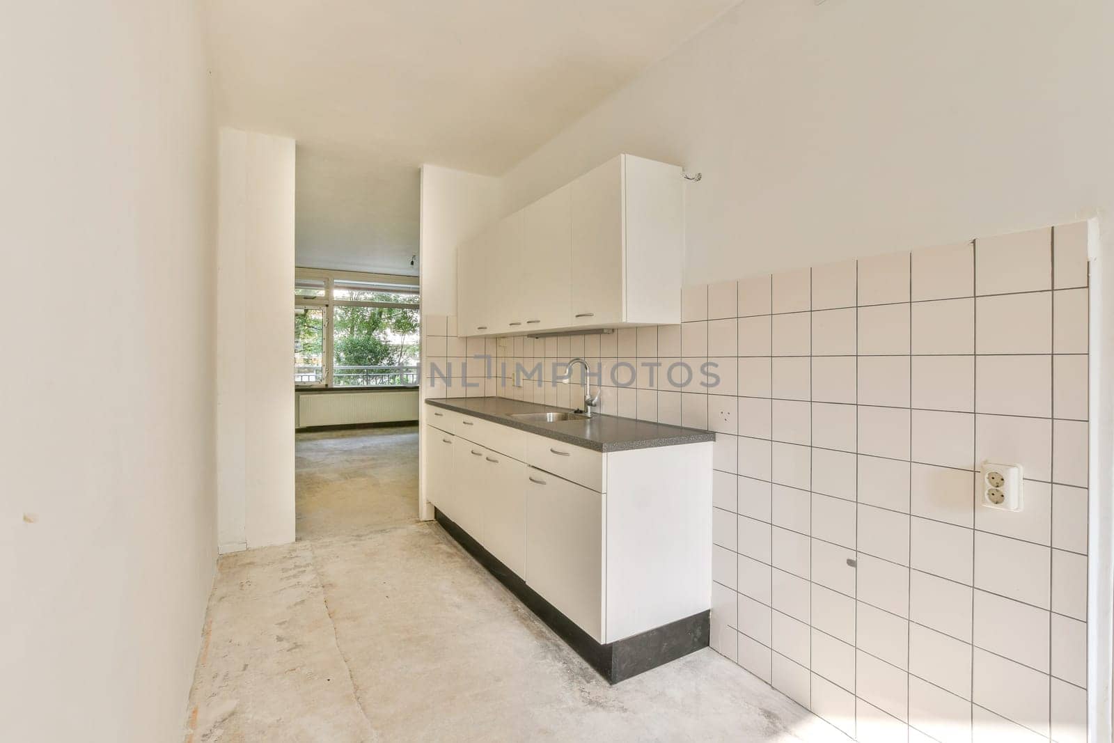 Spacious kitchen area featuring sleek cabinetry, simple countertops, and natural light streaming through large windows, creating a clean and airy atmosphere.