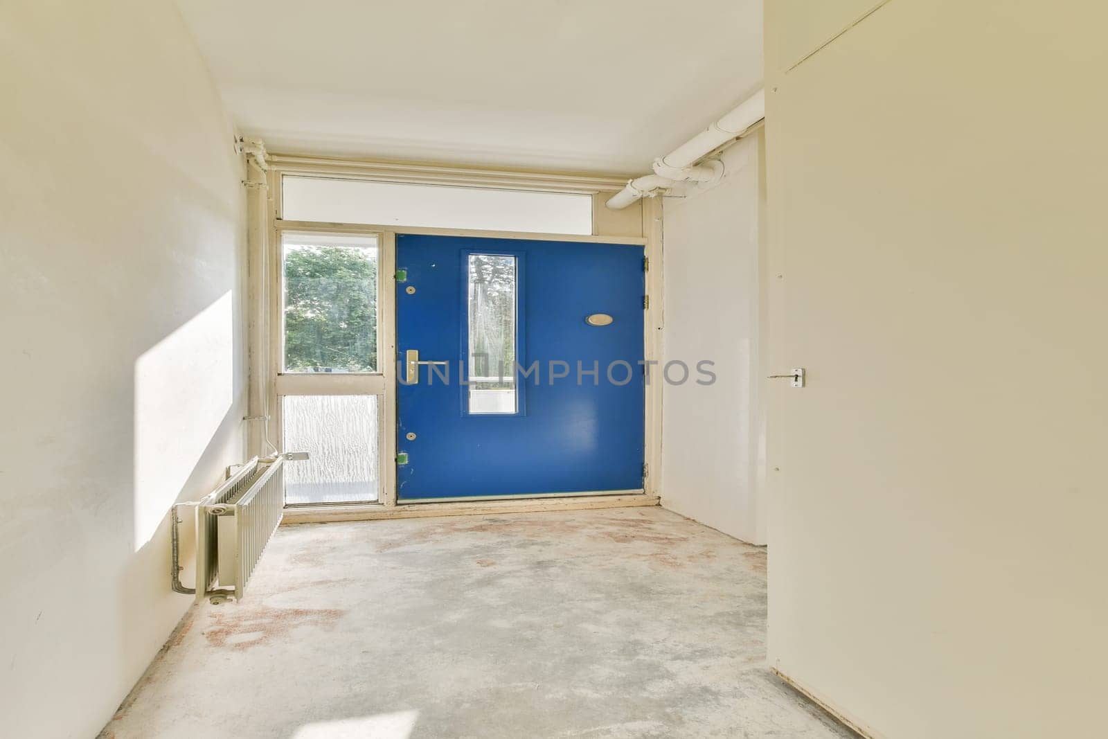 An inviting entrance showcasing a bright blue door against a minimalistic interior design. Sunlight filters in, highlighting the simplicity of the space.