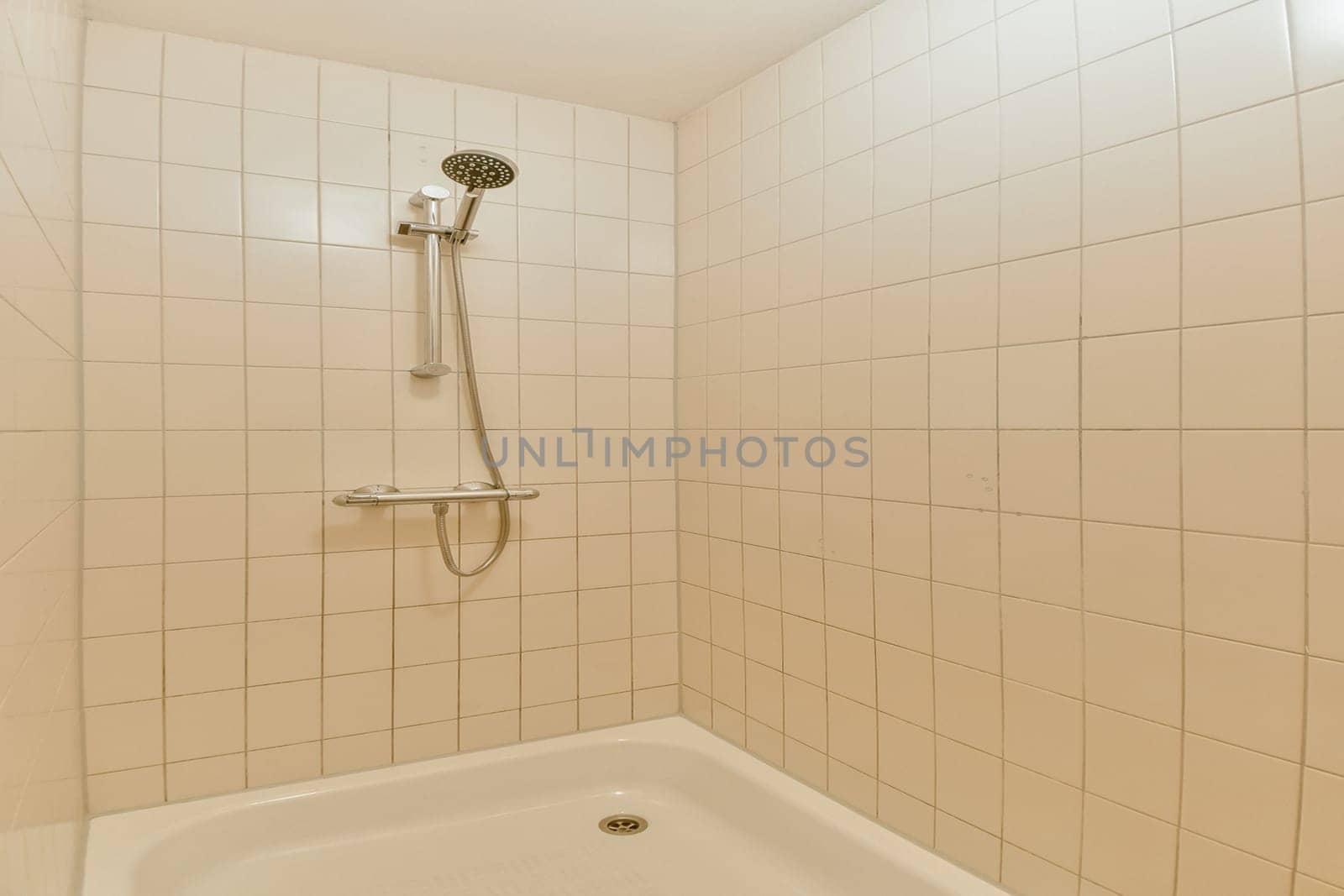 A clean and minimalistic shower area featuring pale tiled walls and a simple showerhead. The design emphasizes a fresh and spacious vibe.
