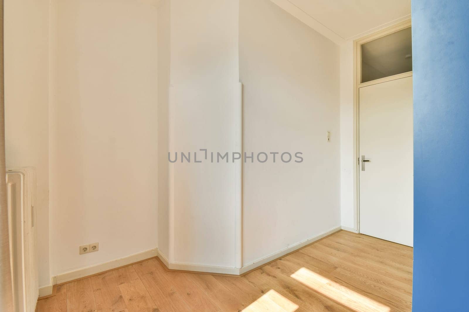 A spacious and bright minimalist room showcasing light walls and wooden flooring. Sunlight streams in, illuminating the simple design elements.