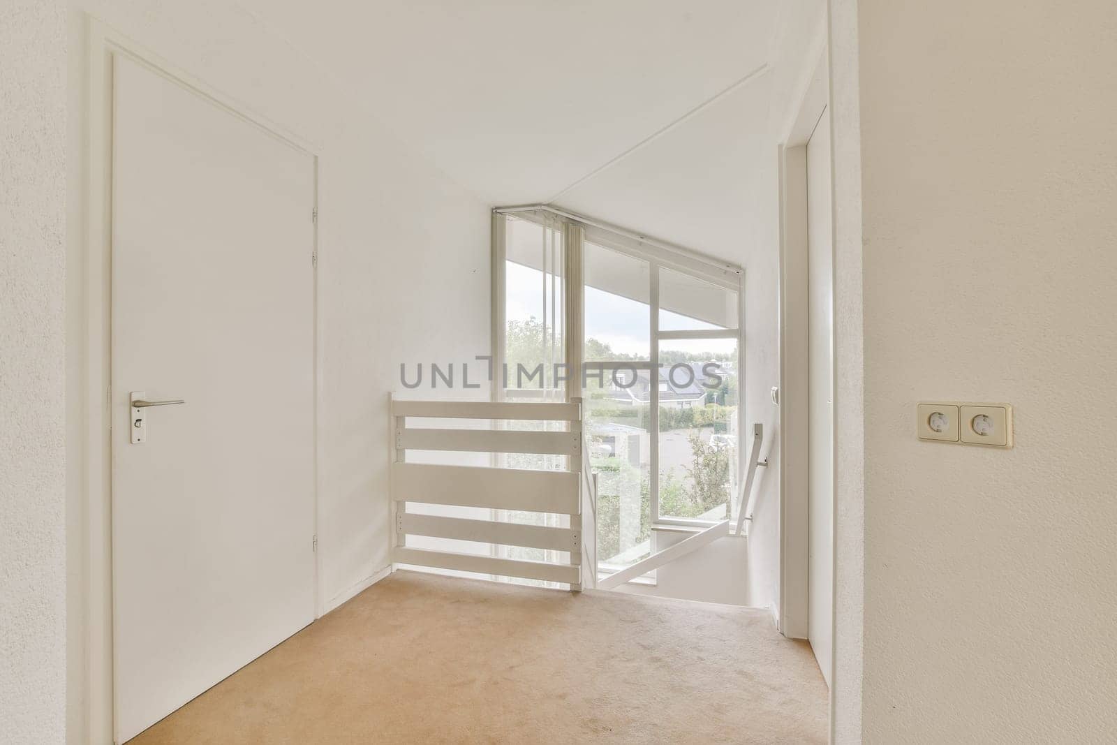 A spacious and well-lit interior hallway featuring a staircase with a modern design and large windows offering a view of the outdoors.