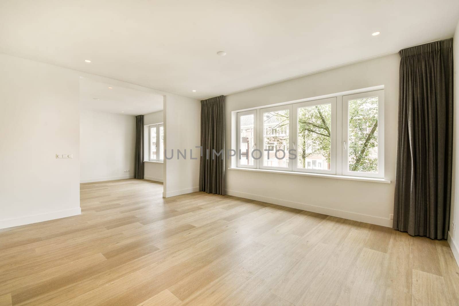 A bright and airy interior space featuring large windows and minimalist design. The floor is wooden, and the walls are painted in a soft, neutral tone.