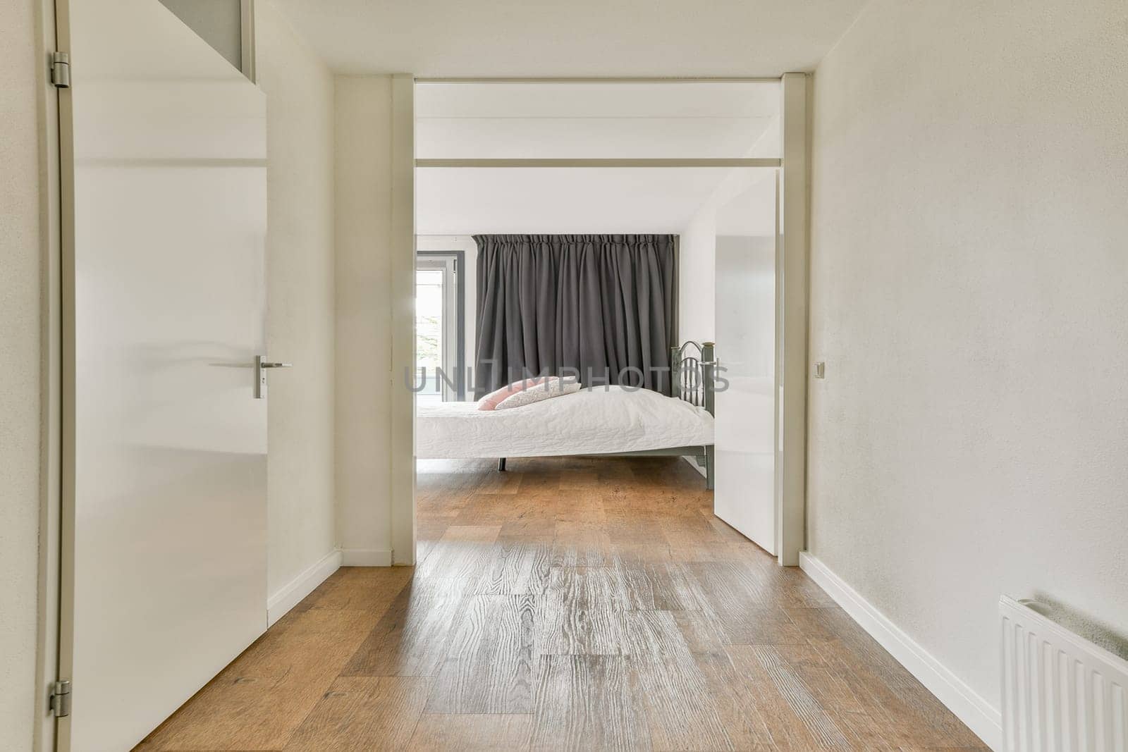 A bright, minimalist bedroom with neutral walls, wood flooring, and natural light flowing through sheer curtains. The calming atmosphere invites relaxation.