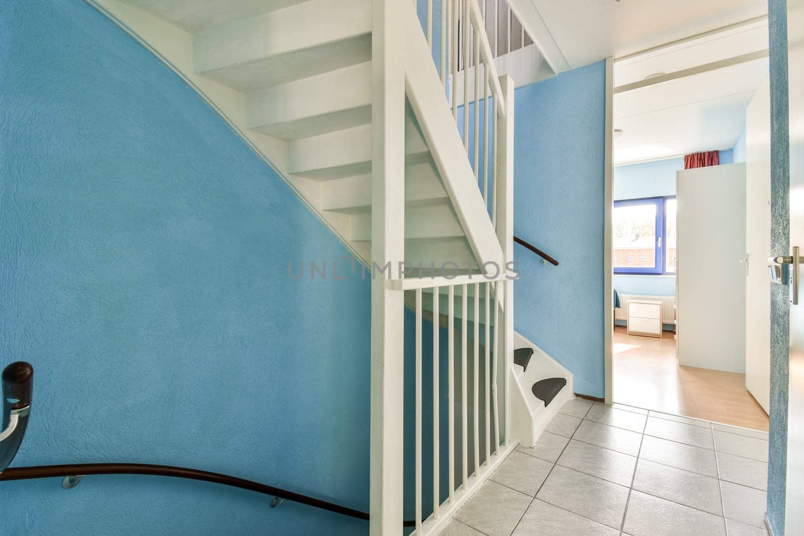 A contemporary interior showcasing a staircase with blue walls, leading to a bright room. The space is well-lit, emphasizing clean lines and modern design elements.