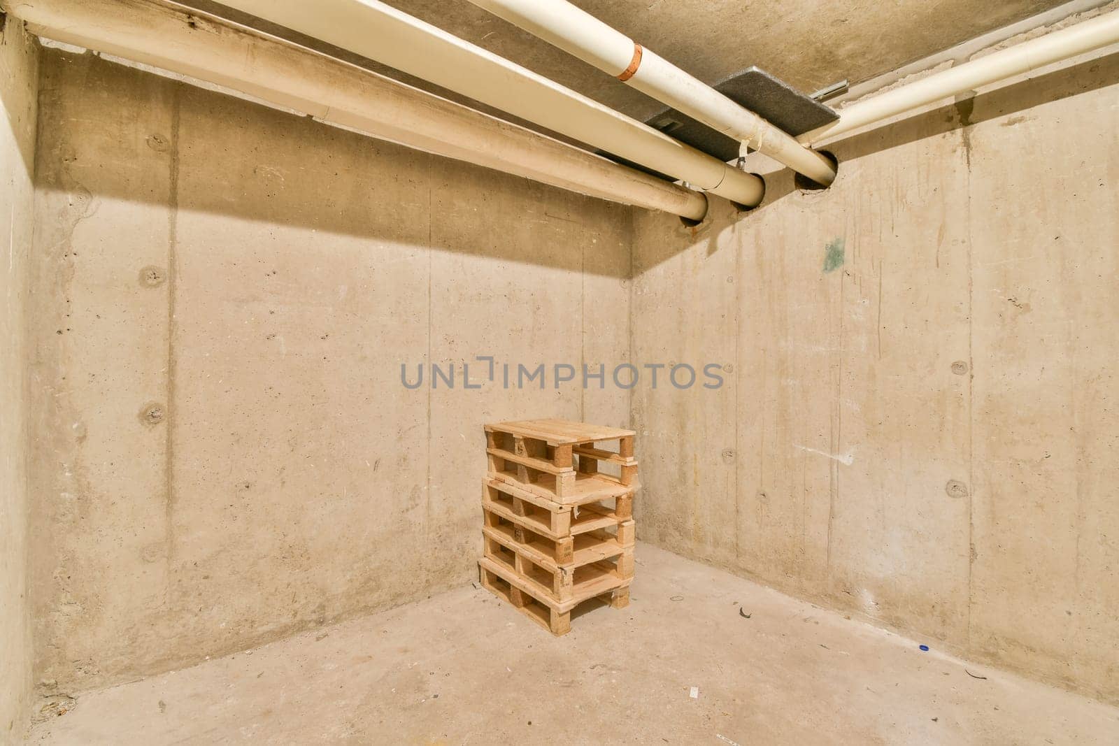 An empty space featuring concrete walls and a wooden pallet positioned in the center, showcasing industrial elements and minimalist design.