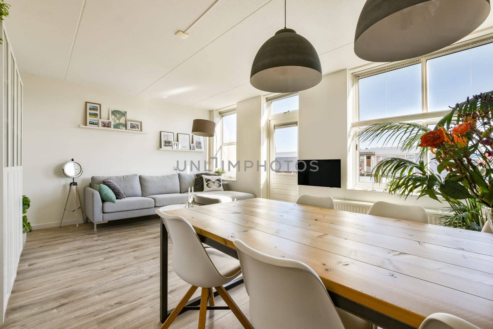 A stylish modern interior featuring a cozy seating area, a dining table, large windows for natural light, and decorative plants, creating a welcoming atmosphere.