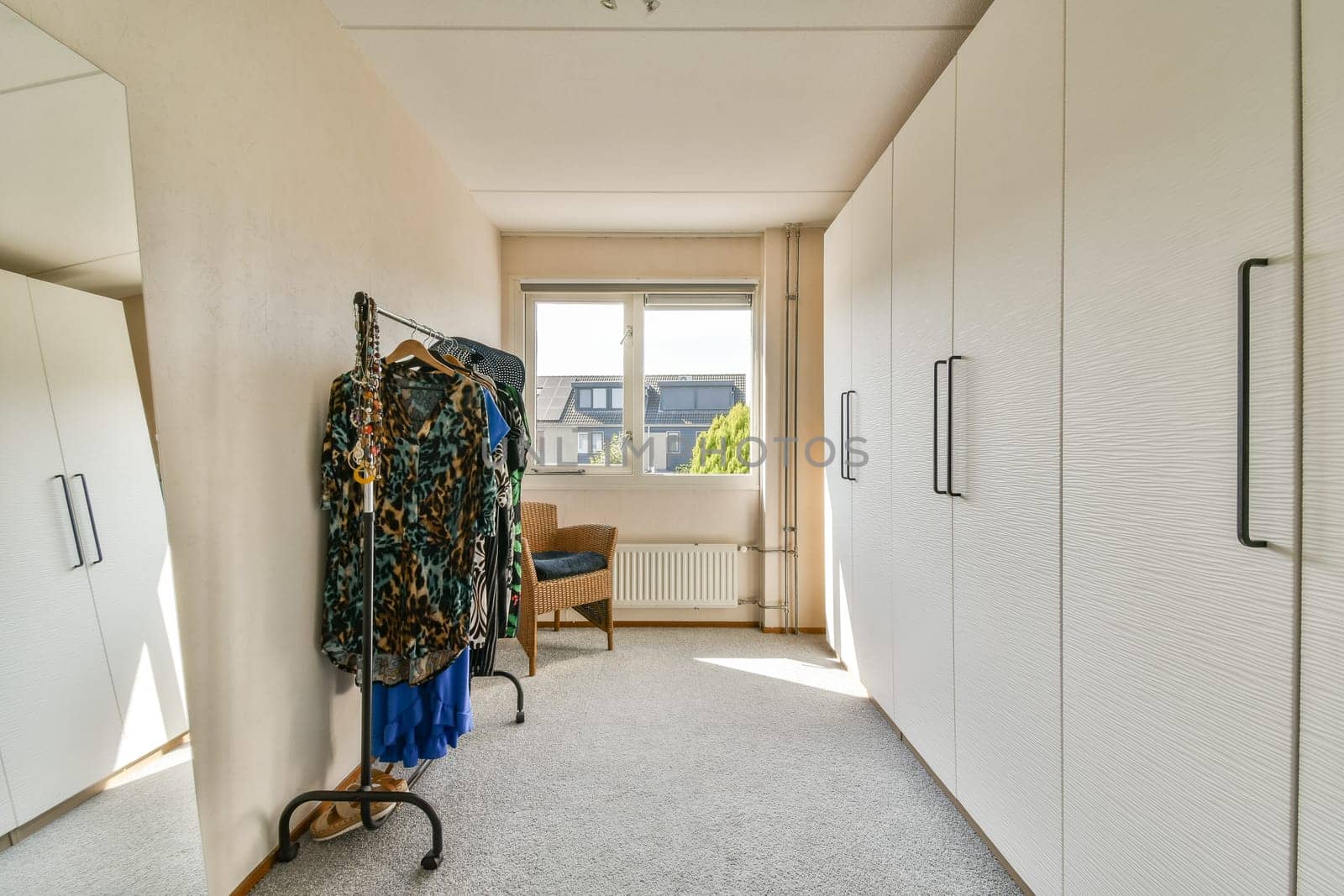 A modern dressing room featuring elegant clothing displays, ample storage space, and bright natural light streaming through the windows.