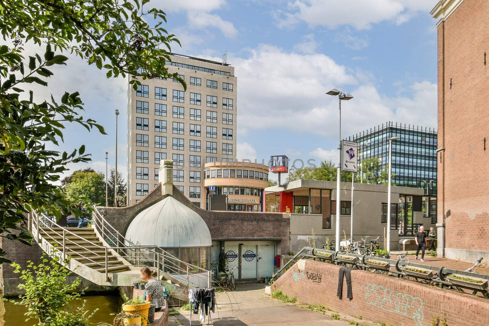 A vibrant city scene showcasing contemporary buildings, pedestrian areas, and lush greenery beside water, merging nature and urban life seamlessly.