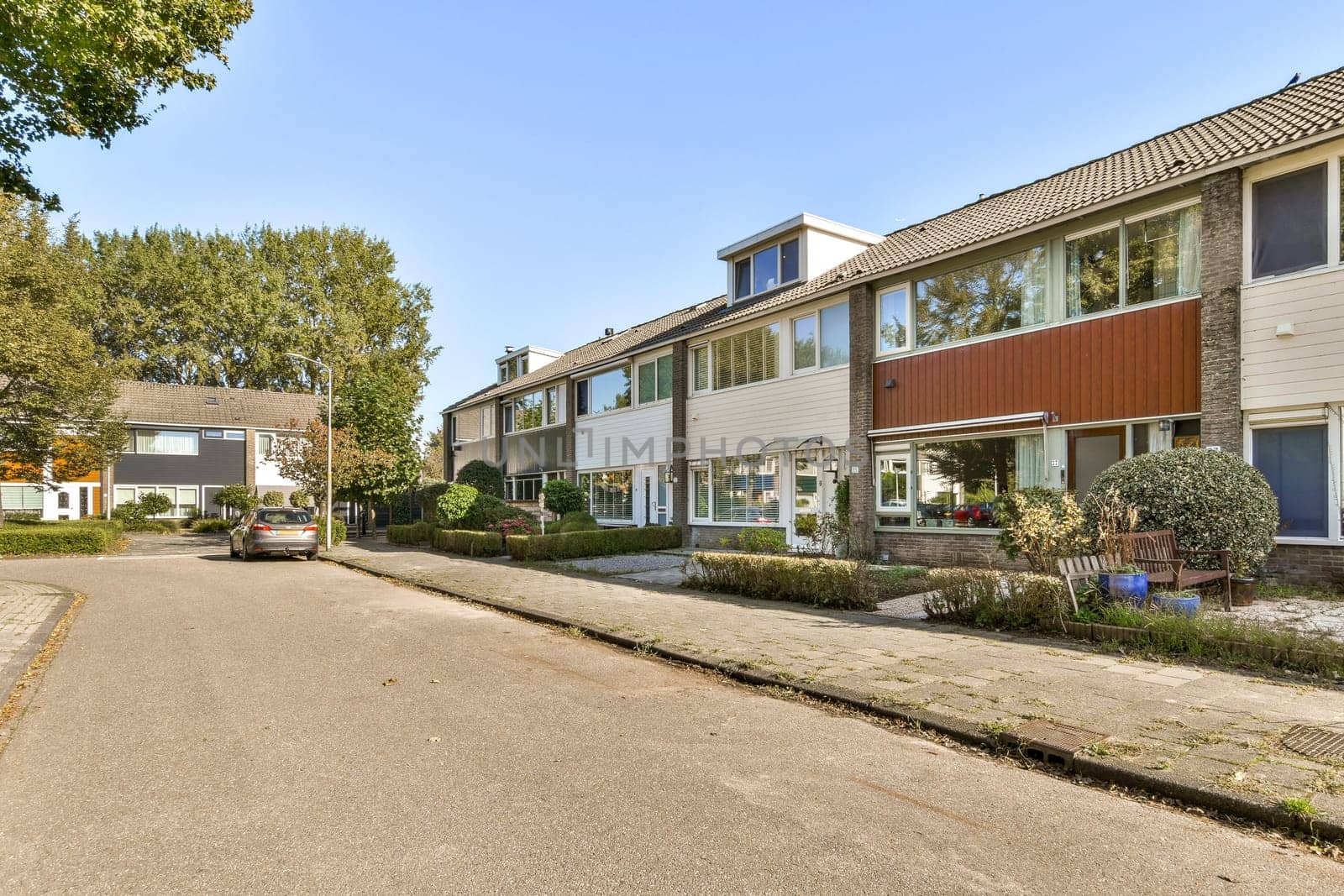 A picturesque suburban street featuring modern residential buildings, lush greenery, and parked cars under clear skies. Ideal for showcasing contemporary architecture.