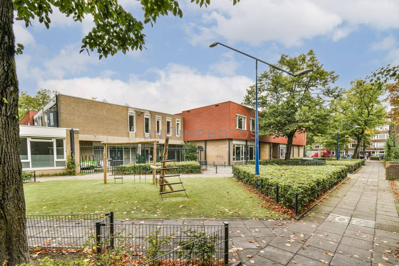A serene view of a modern residential area featuring a playground amidst lush green grass and trees. The architecture blends well with the surroundings.