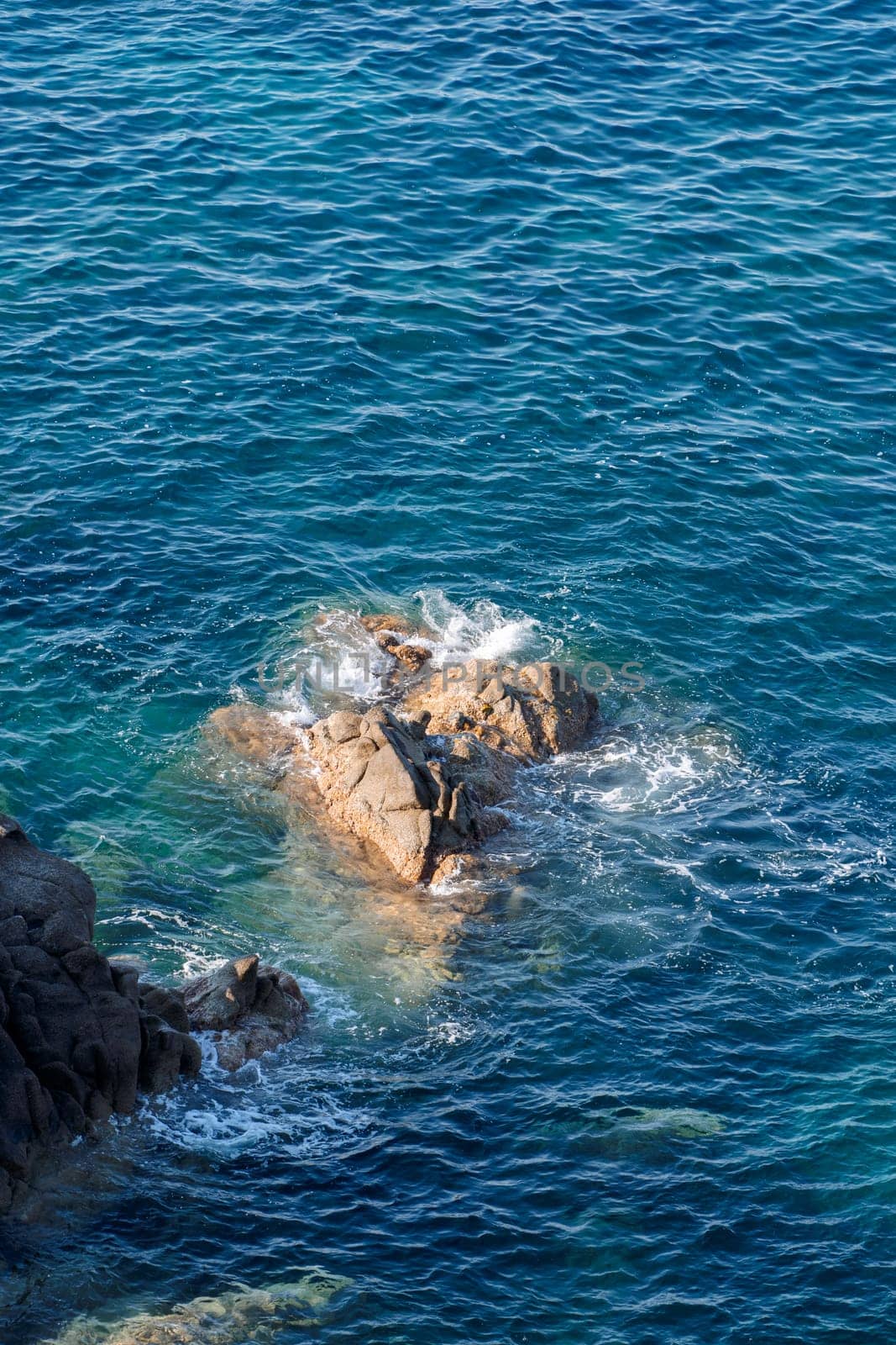 Wild rocky beach coastline and the sea, wave splashes on rock in sea shore, calm sea. Breaking waves to the rocks on shore creating white sea foam and small bubbles, top view