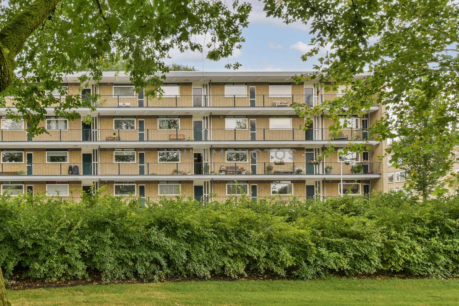 A contemporary residential building features multiple balconies and large windows, blending with lush greenery in the foreground, showcasing urban living.