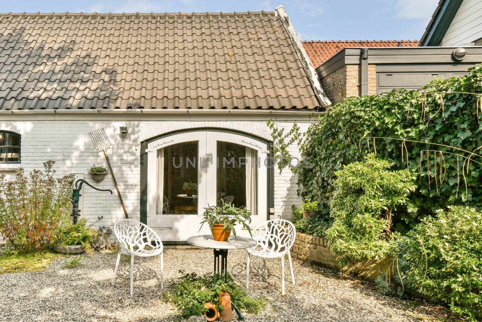 A cozy outdoor patio featuring white chairs and a small table surrounded by lush green plants. The inviting space is ideal for relaxation and leisure moments.