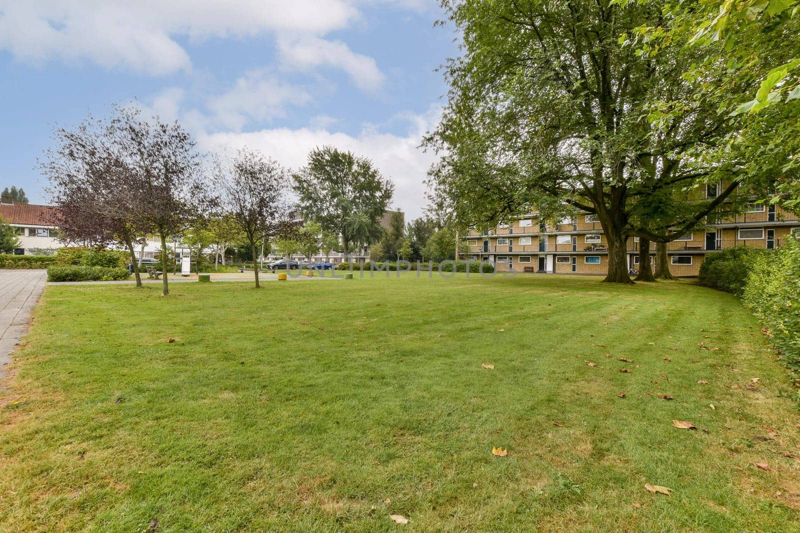 A picturesque park setting featuring neatly manicured grass, trees, and a backdrop of contemporary buildings, offering a serene escape in an urban environment.