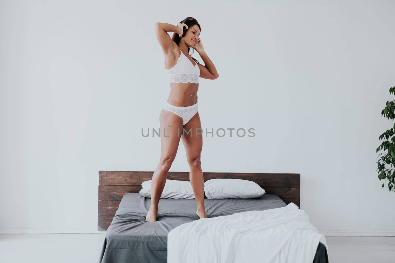 Brunette in lingerie listening to music in headphones and dancing in bedroom on bed