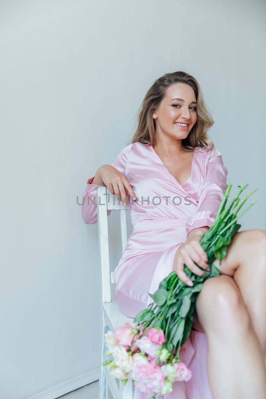 Fashionable woman in summer pink dress with bouquet of spring flowers sitting on chair