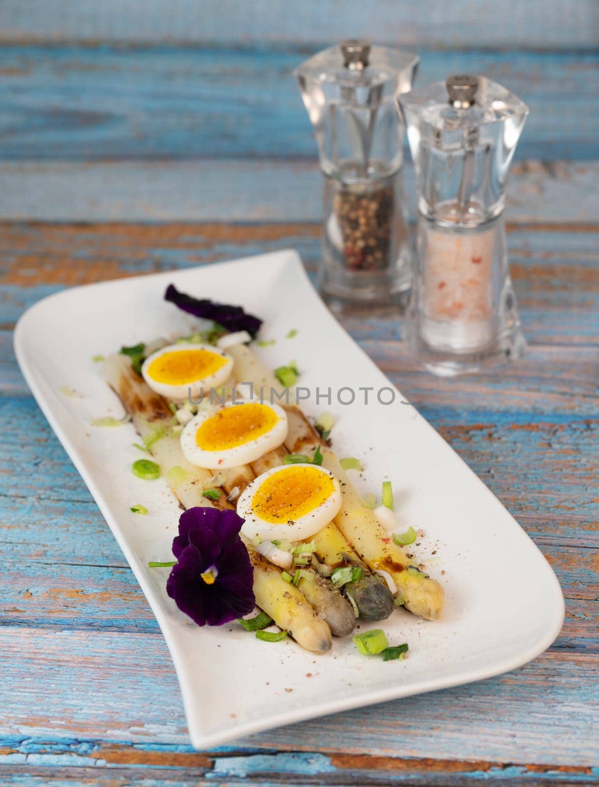 Baked asparagus with boiled egg in big white plate on blue background. High quality photo
