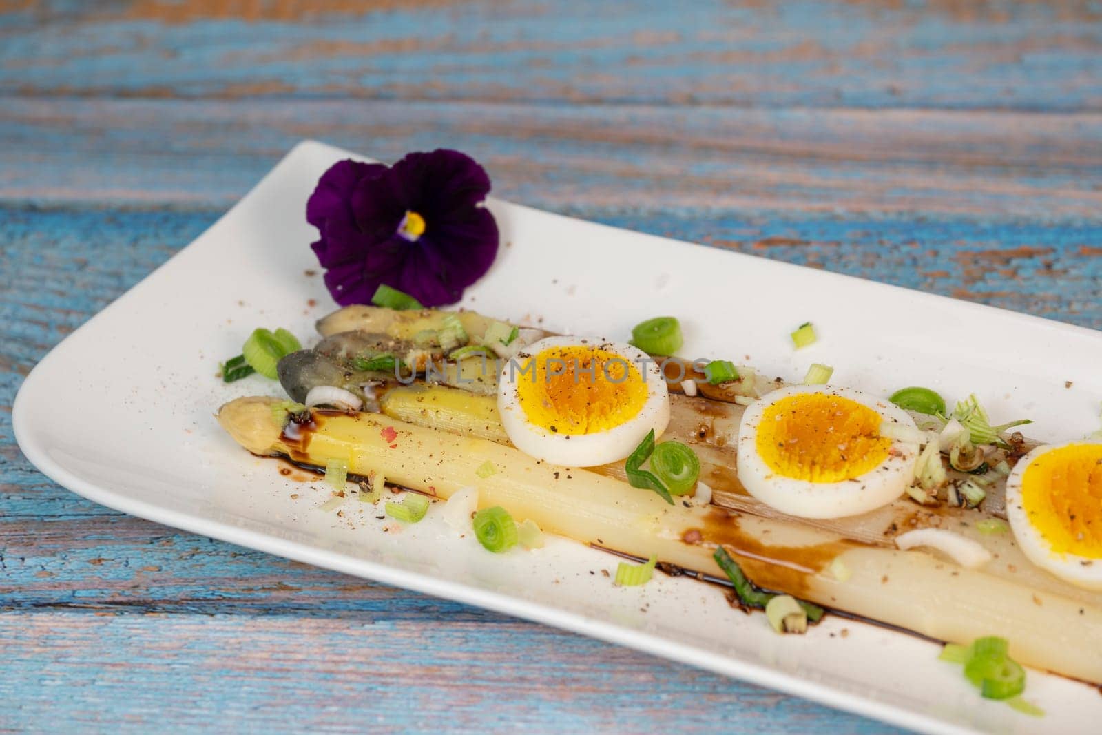 Baked asparagus with boiled egg in big white plate on blue background. High quality photo