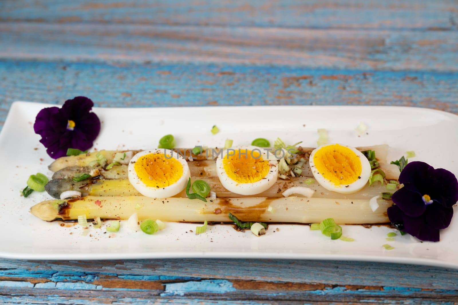 Baked asparagus with boiled egg in big white plate on blue background. High quality photo