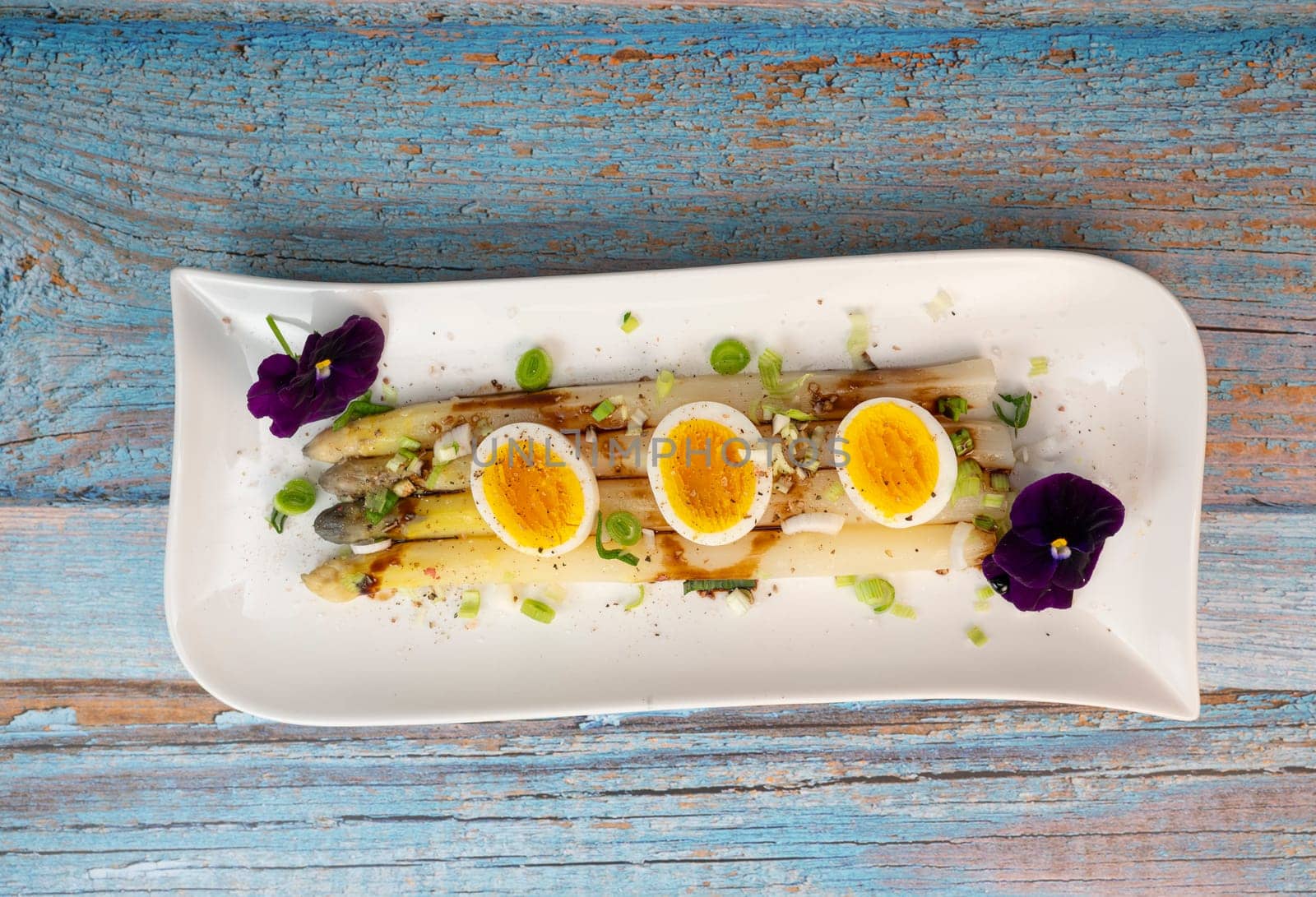 Baked asparagus with boiled egg in big white plate on blue background. High quality photo