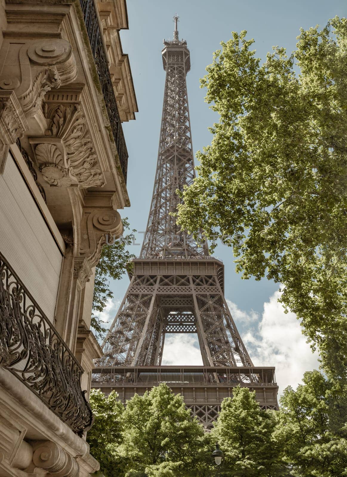 France, Paris - May 03, 2025 - The Ultimate Eiffel Tower View from on Rue de L’Universite in Paris. A back alley in Paris showcasing the architecture of Eiffel Tower view between with trees and typical parisian buildings in the foreground in Rue de l'Universite street, 7th arrondissement, use it as your Wallpaper, Poster and Space for text, Selective focus.