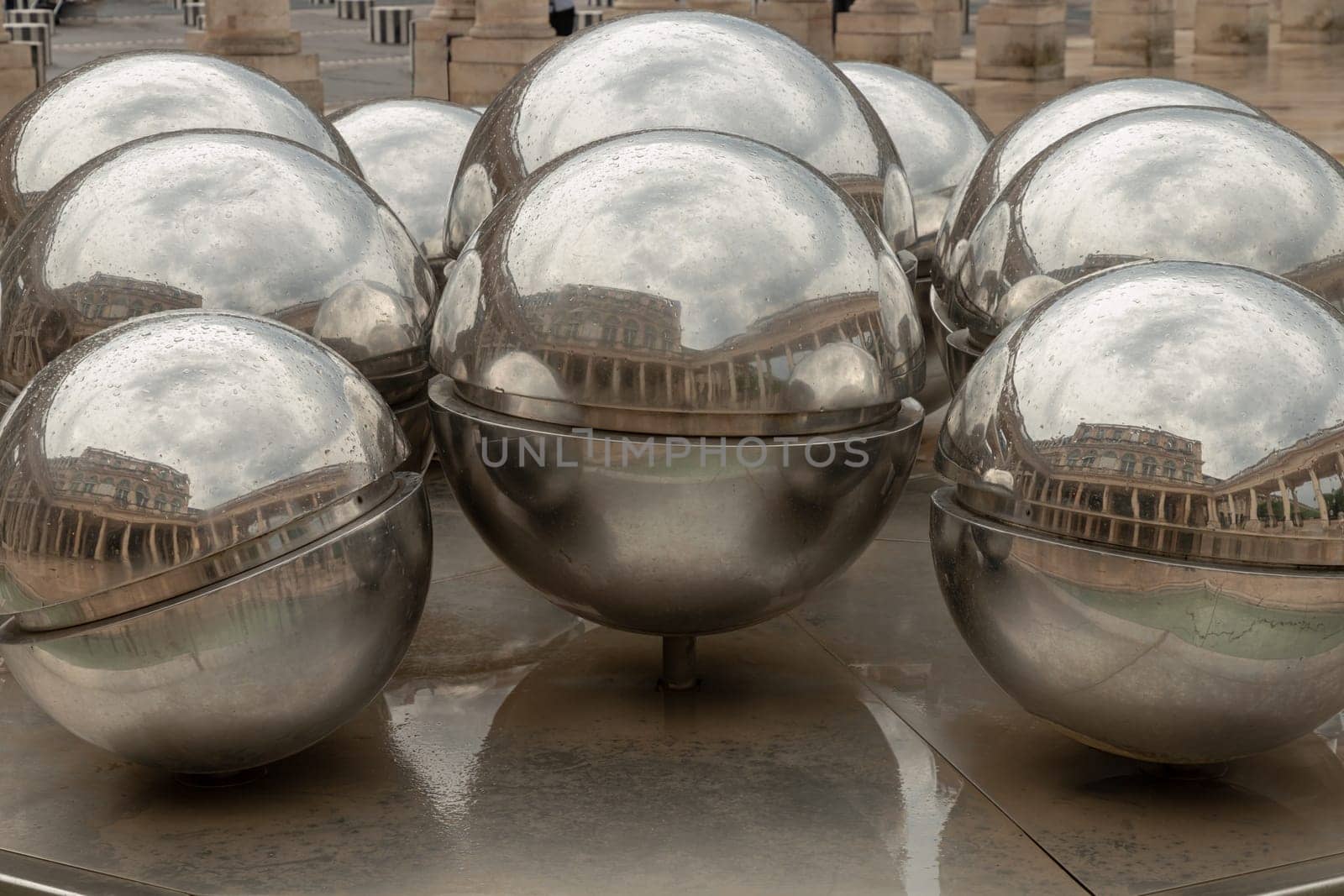 France, Paris - May 03, 2025 - View of 10 stainless steel spheres on Fontaines de Pol Bury (La Fontaine des Spheres) that slowly rotate on their axis, propelled by the flow of water cascading over them with reflecting the passersby in the court of Honor at the Palais-Royal. use it as your Wallpaper, Poster and Space for text, Selective focus.
