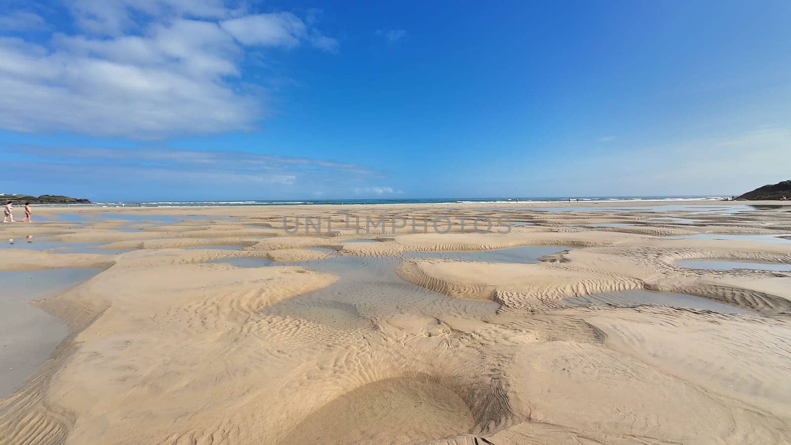 A serene and tranquil beach view showcases intricate sand patterns at low tide, all beneath a clear blue sky
