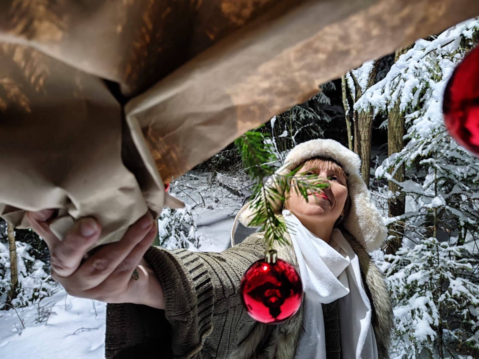 A funny middle-aged woman strolls through a snowy forest at night, engaging in a whimsical activities with holiday decorations.