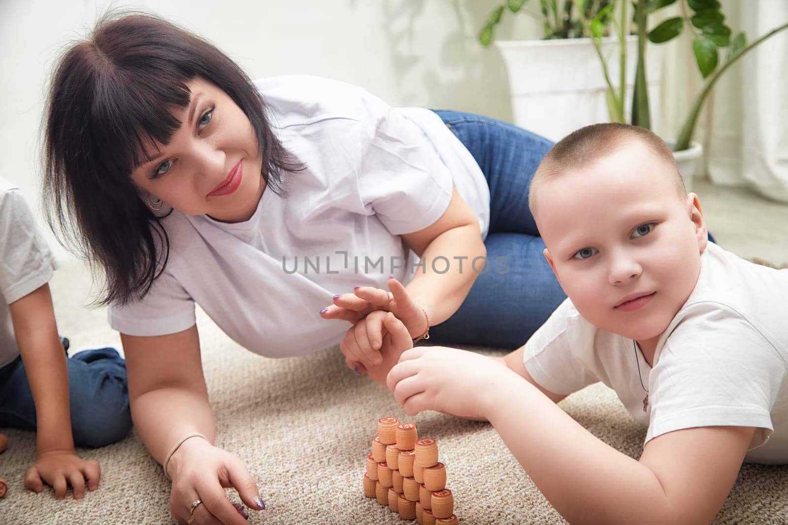 A woman and a boy are engaged in a stacking game with cups while two children play nearby, enjoying quality family bonding.