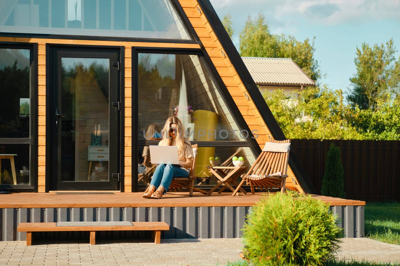 Mid adult woman sitting with laptop on the terrace of a-frame cabin