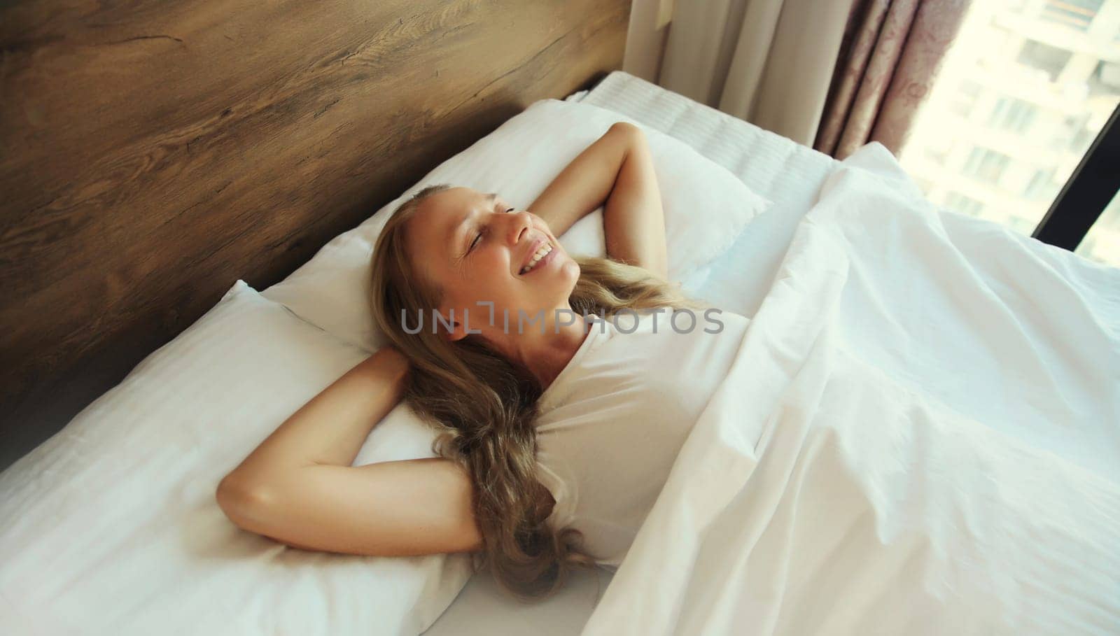 Happy young woman sleeping lying in bed on white soft comfortable pillow in bedroom at home