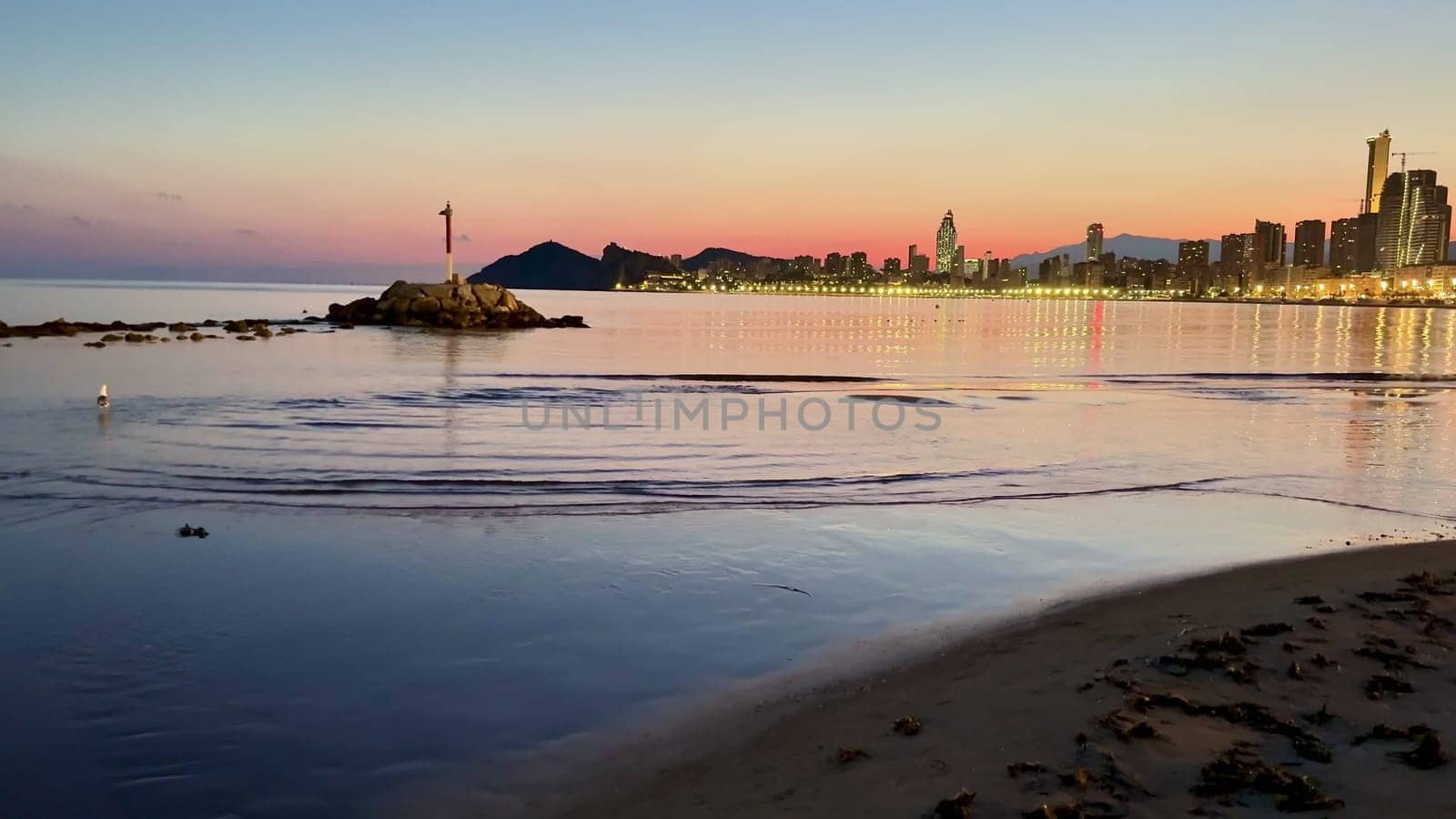 A serene twilight view of a coastal city, with reflections in calm waters and a stunning, colorful sky