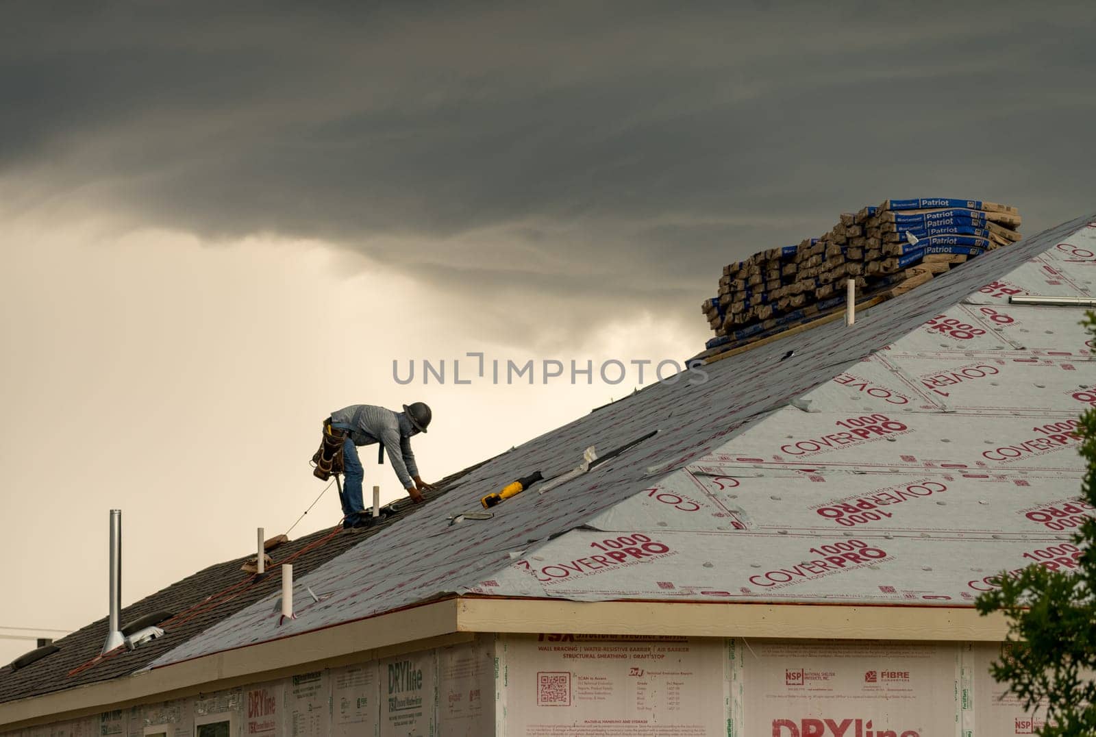 Georgetown, TX - 5 May 2025: Roofer installing shingles on roof of new home during thunderstorm and severe weather