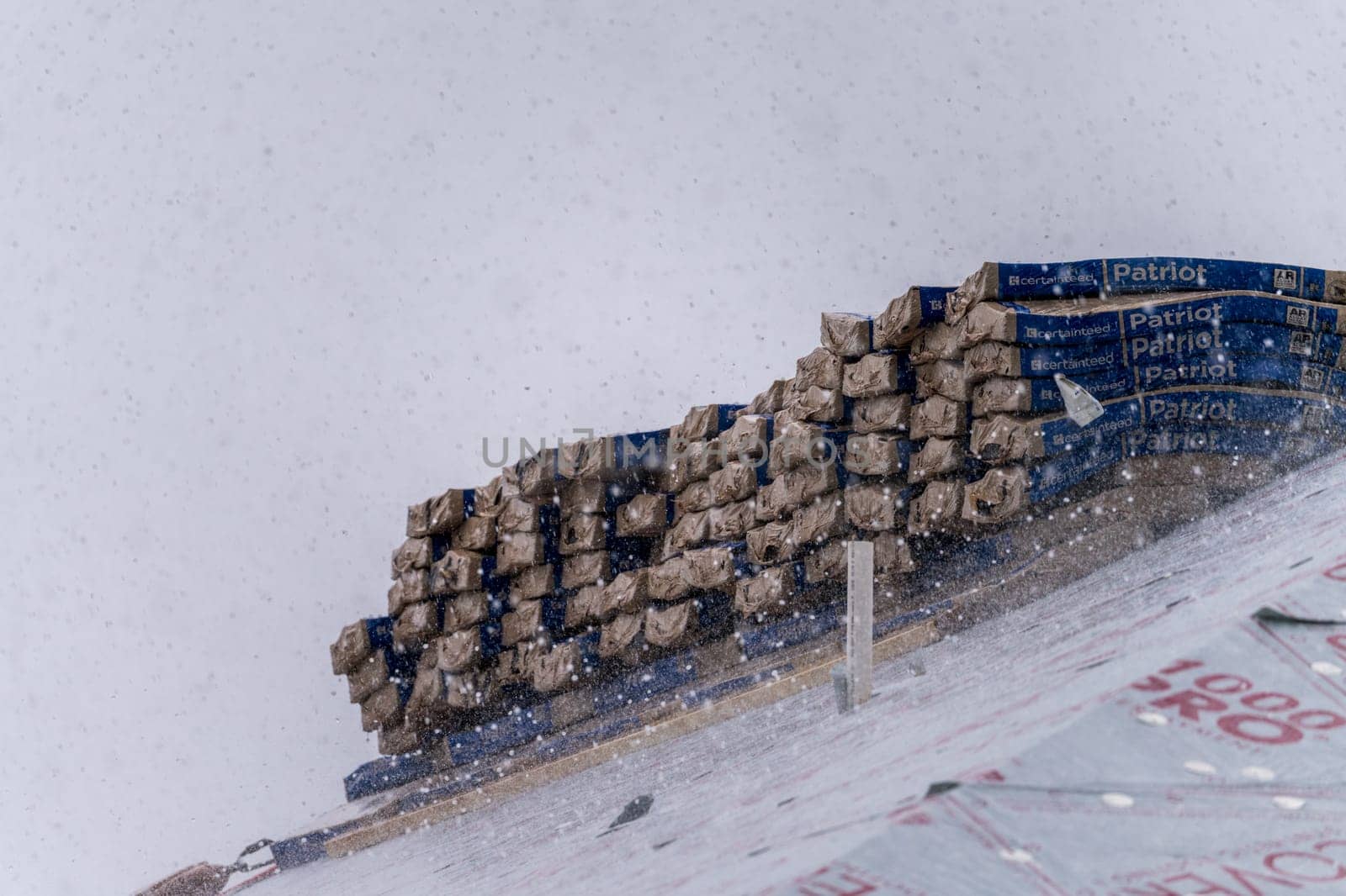 Georgetown, TX - 5 May 2025: Stack of Patriot shingles on roof of new home during thunderstorm with severe hailstones
