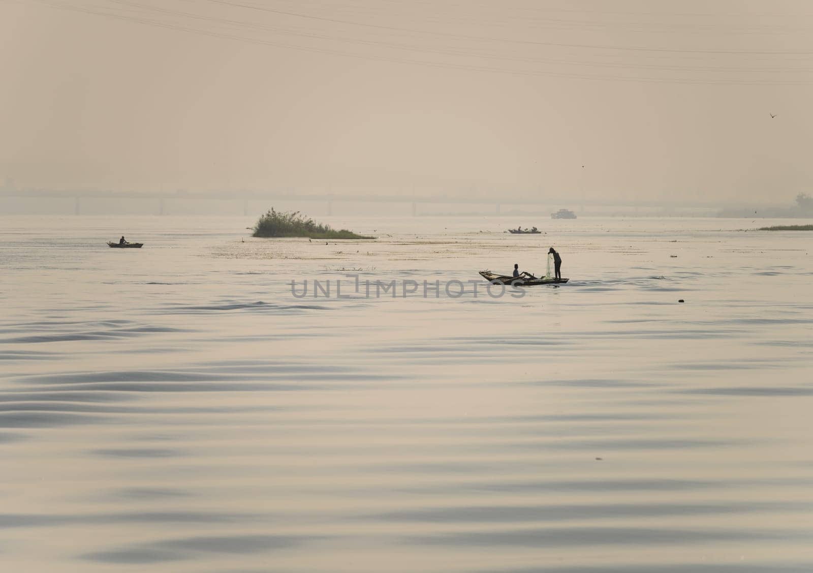 Two men in their small boat on a calm river Nile while tending to fishing net in the water as dusk approaches