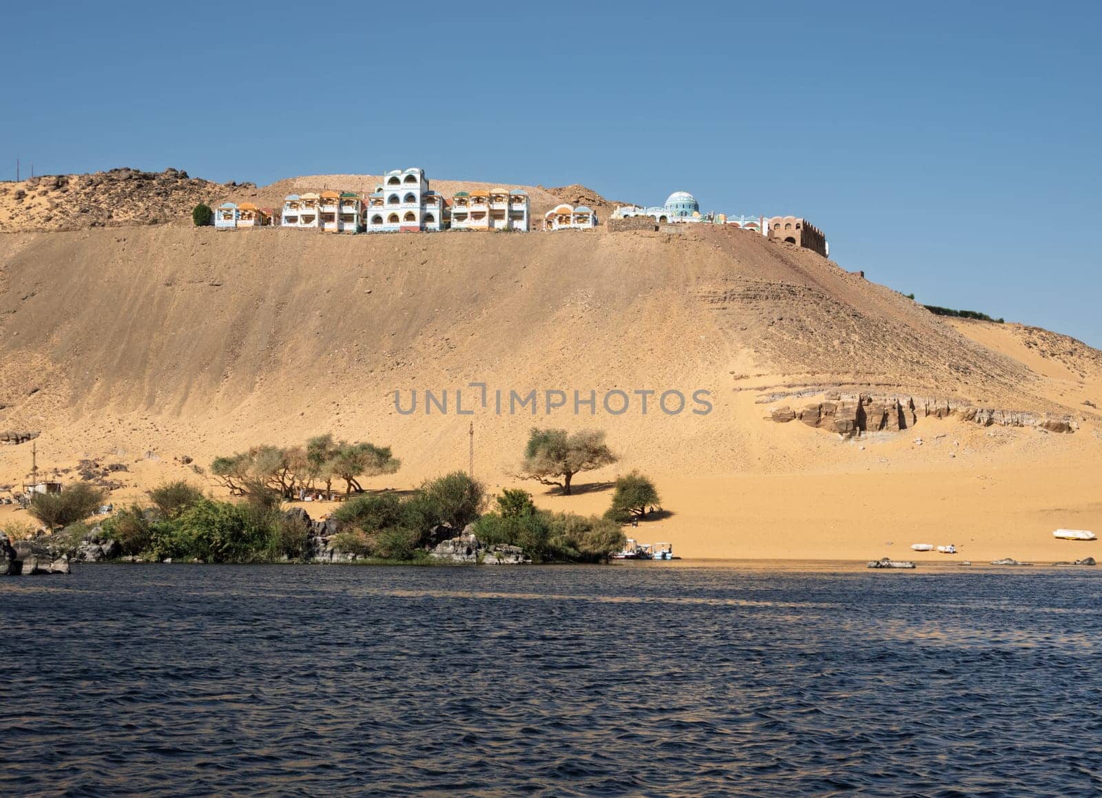 Fast flowing water of the River Nile near Aswan Egypt with Nubian vacation resort on hilltop
