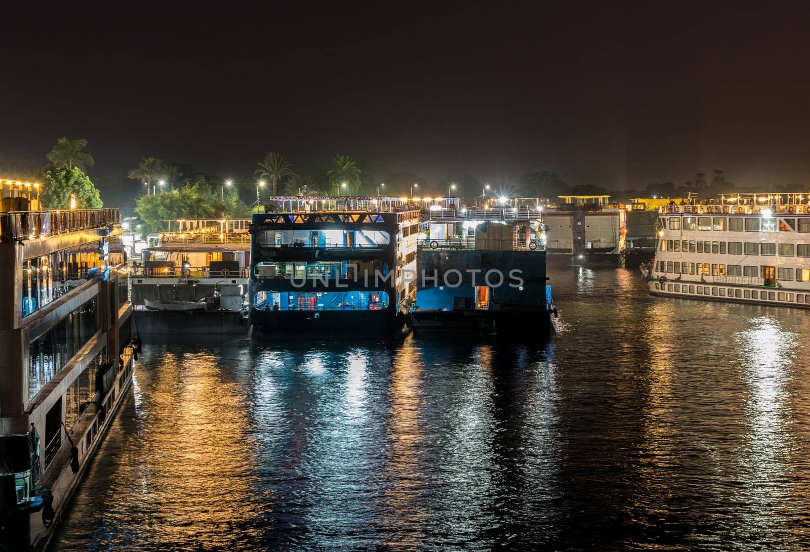 Illuminated Egyptian Nile cruiseboats stacked along the riverbank at Kom Ombo for temple visit