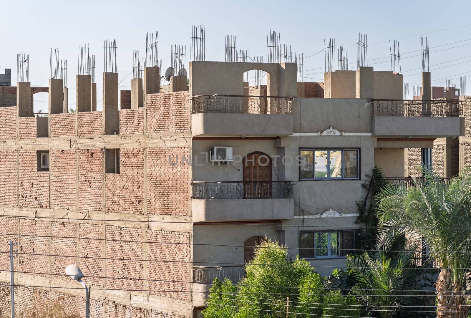 An unfinished building in Esna, Egypt, with brick and concrete construction and rebar on roof. Some apartments occupied