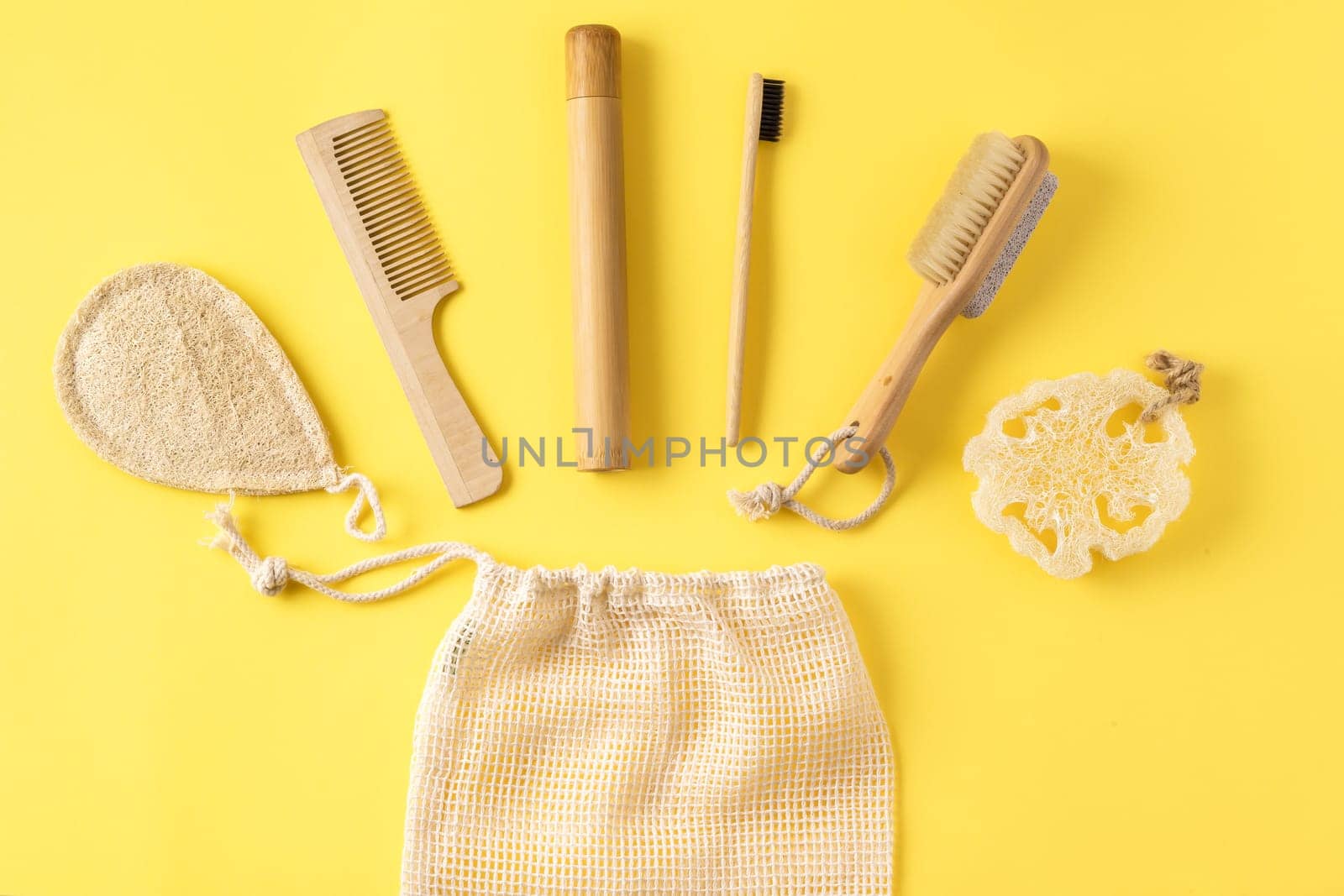 Zero waste concept. Anti cellulite massager, bamboo toothbrush, loofah sponge, peeling brush, wooden comb and produce bag on pastel yellow. Top view, creative layout. Set of bathroom accessories.