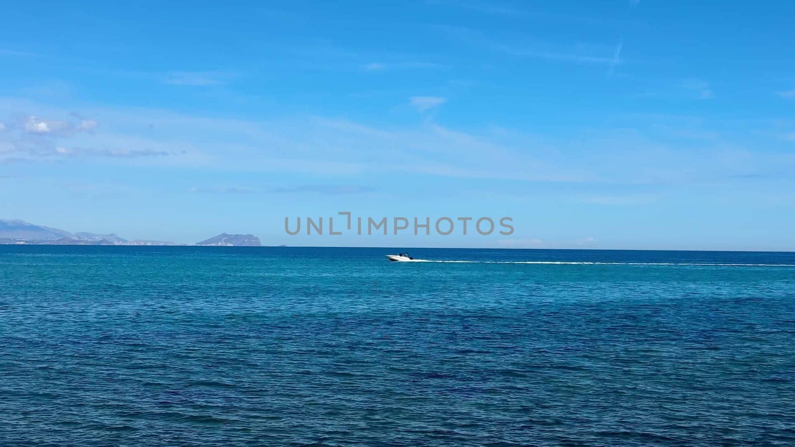 A sleek, fast speedboat glides effortlessly through the crystalline blue waters under a bright, clear sky