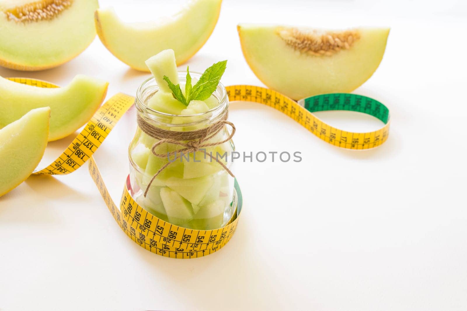 Left a jar with melon pieces on burlap napkin near cut slices of melon and centimeter right empty place for text on a white background. Pieces of melon in a jar. Horizontal. Daylight.