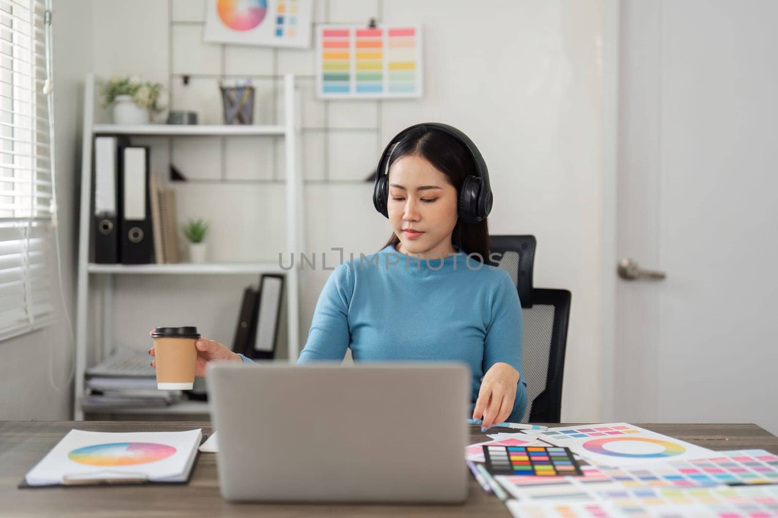A focused graphic designer immersed in her work, sipping coffee and contemplating creative concepts at her stylish desk, surrounded by vibrant color palettes.