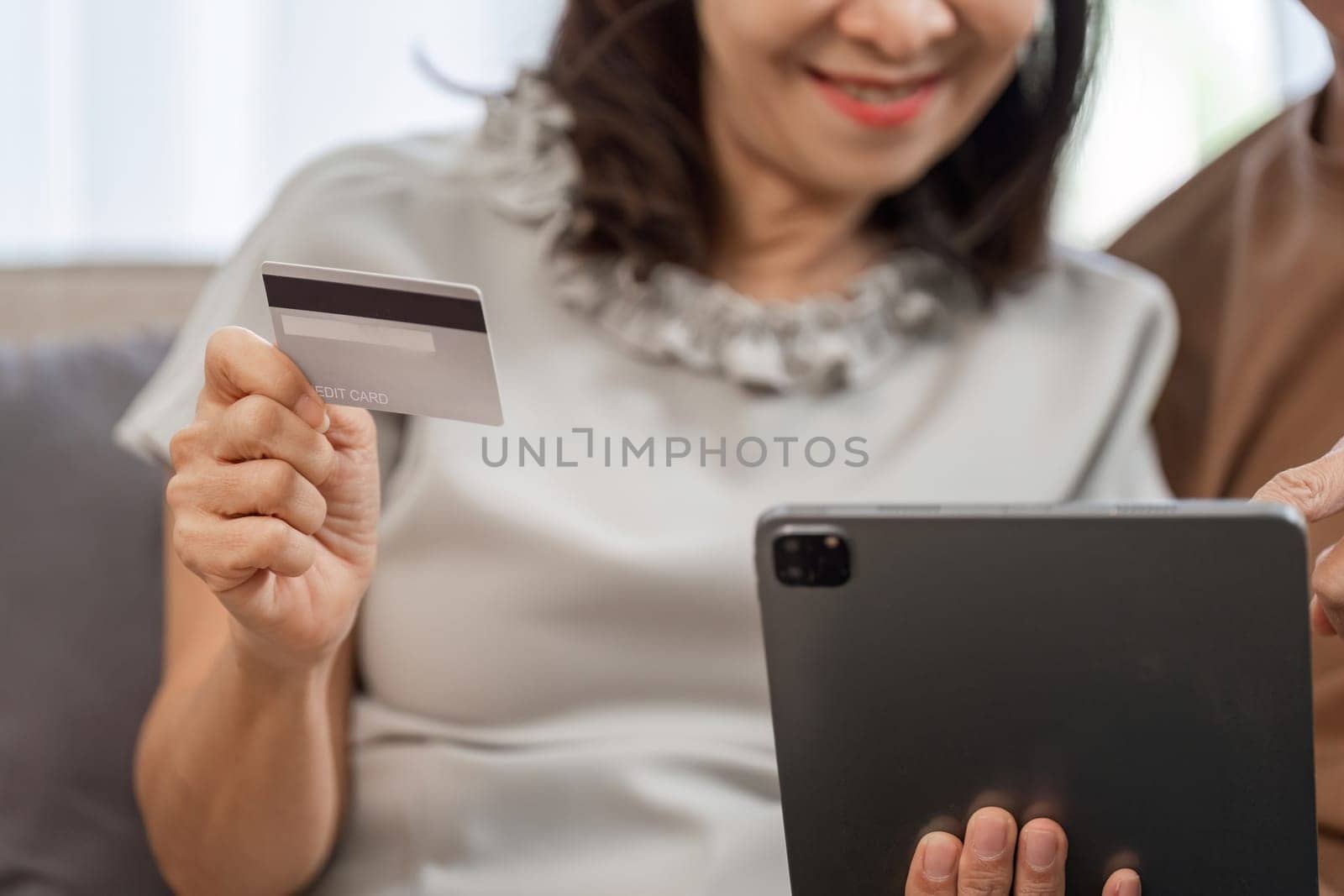 Senior couple happily shopping online using a tablet and credit card, embracing modern technology in the comfort of their home.