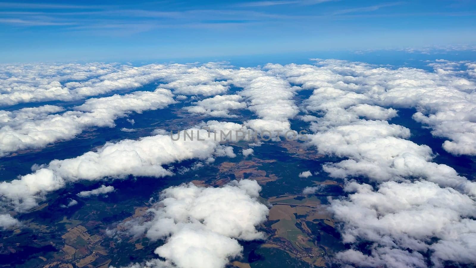Aerial shots beautifully showcase fluffy white clouds floating high above vibrant green fields beneath a clear blue sky
