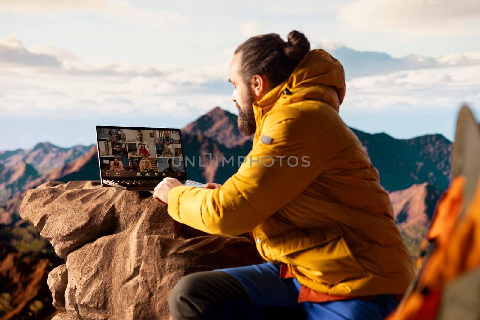 Young nature lover businessman meeting with colleagues on online video call, enjoying high speed internet and connectivity on top of the mountain. Male hiker entrepreneur with dependency.