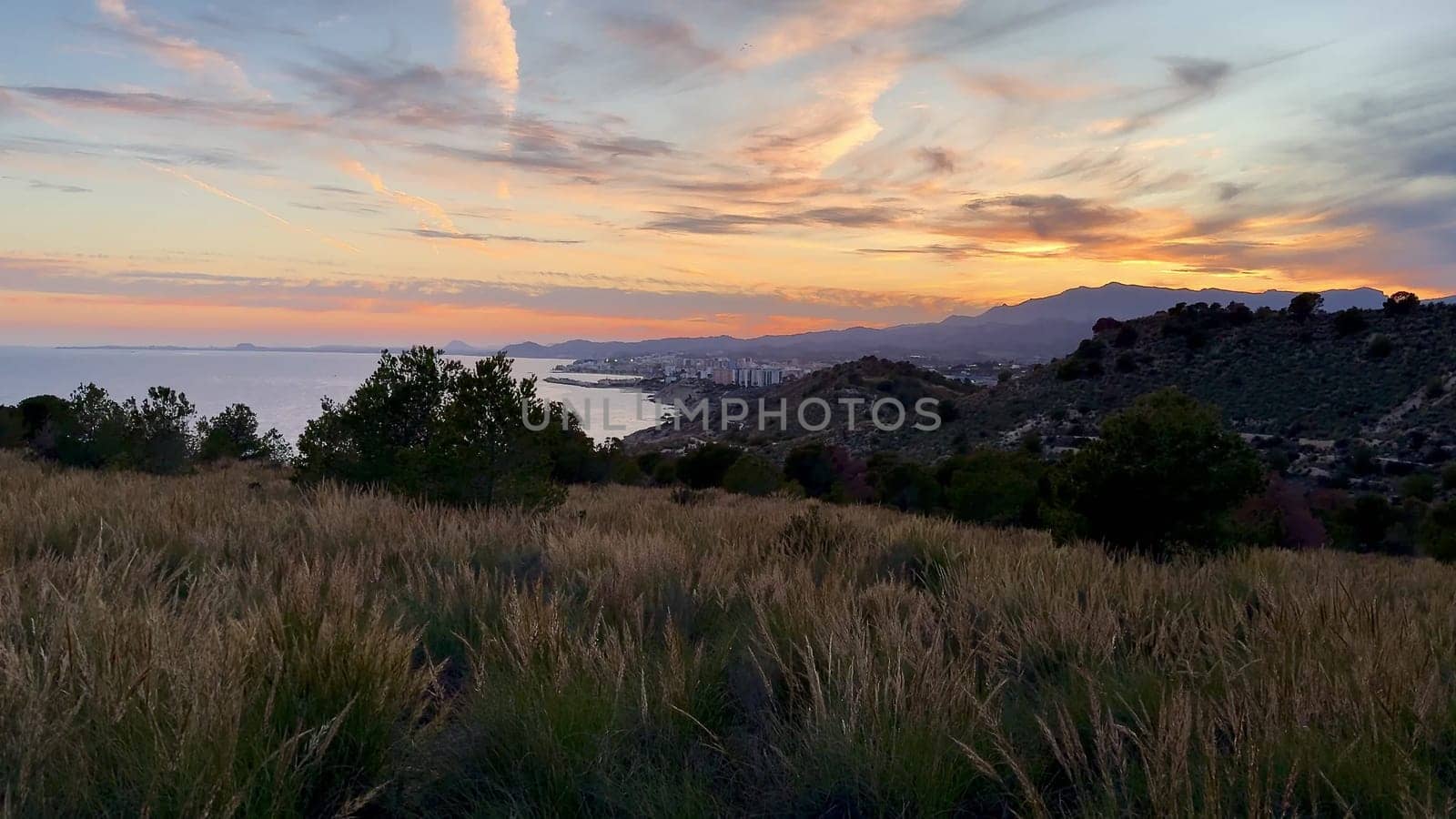 Enjoy the stunning sunset view shimmering over the coast, hills, and vibrant green fields around you